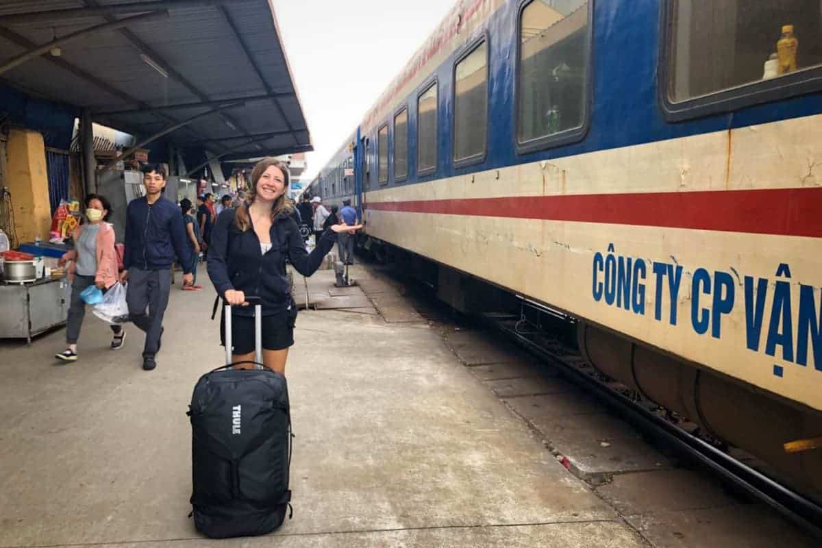 Eine Reisende steht am Bahnhof von Hue in Vietnam neben einem Zug